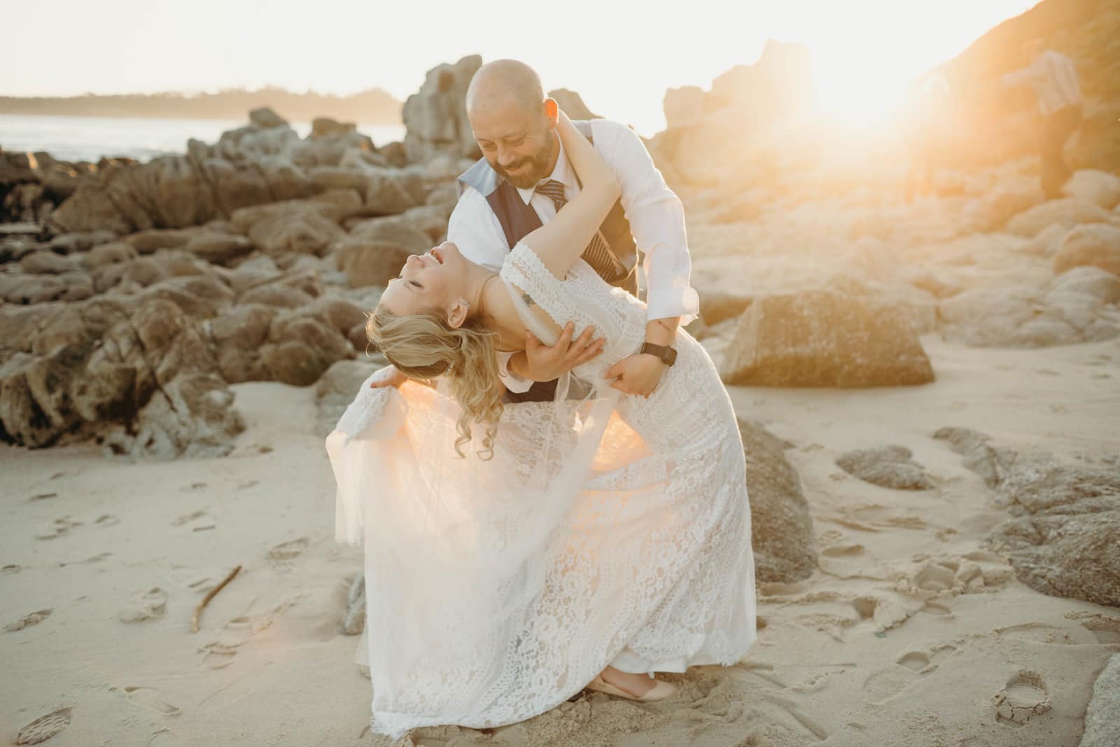 A groom dipping his bride after their beachside elopement at Carmel River State Park in Lake Tahoe