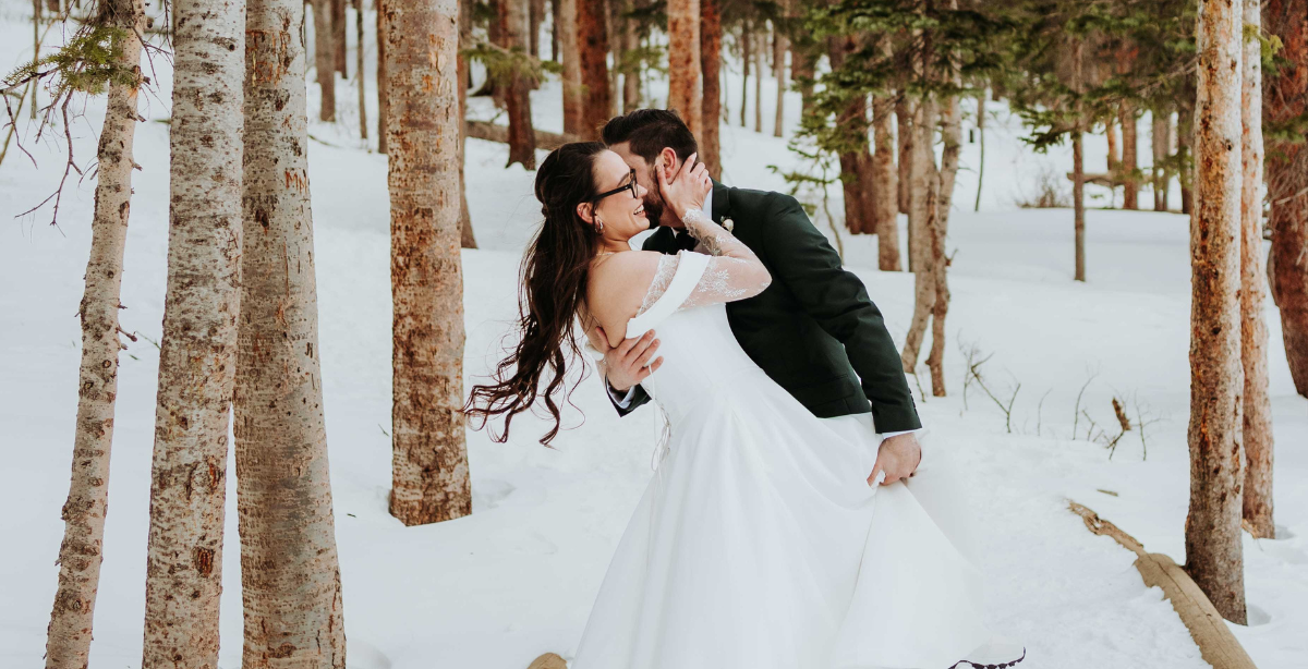 Groom dips bride in snowy Rocky Mountain National Park after their elopement ceremony.