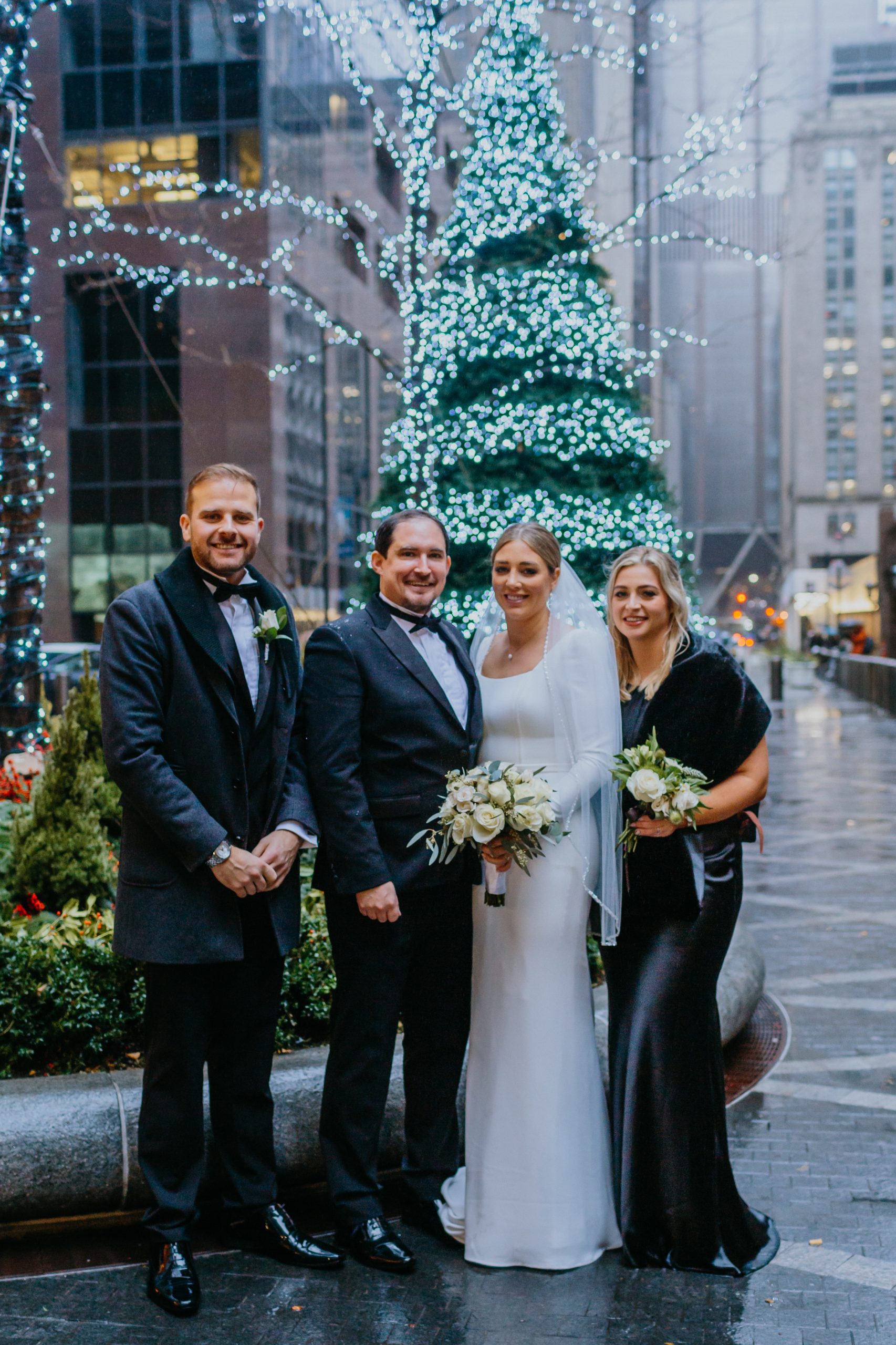 Couple poses with their siblings in front of a christmas tree.