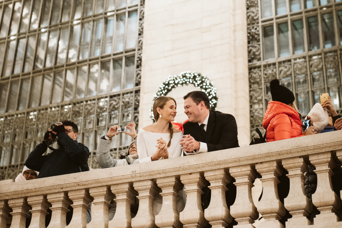 Couple leans over railing while laughing together at Grand Central Station after their New York winter wedding.
